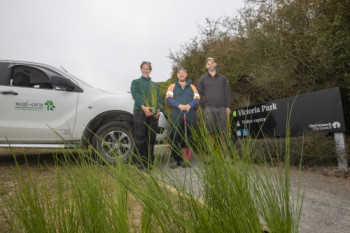 three people stand near a ute parked near some bushes