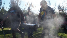 Three men carrying a tray of food for a hangi