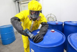 worker in protection clothing filling a large drum with a hazardous substance