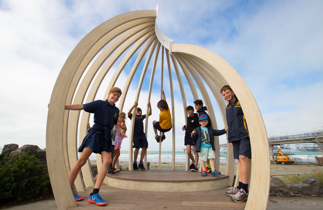 Children pose inside a shell shaped wooden structure