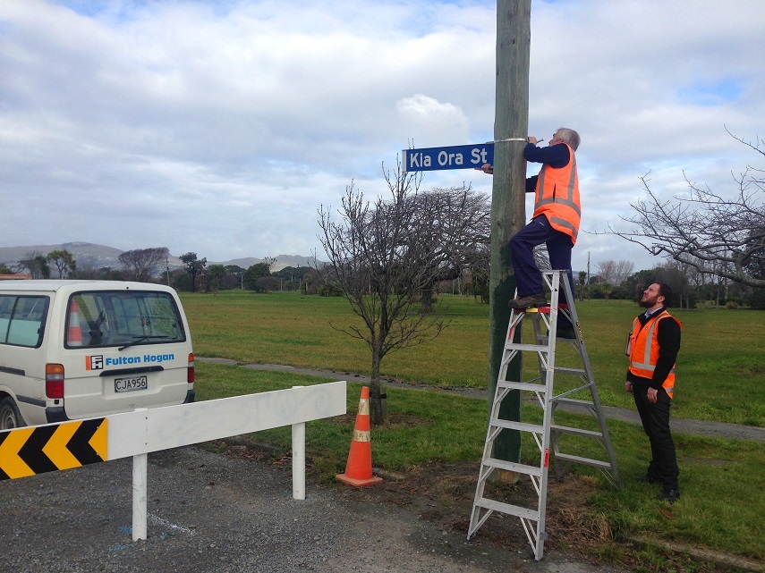 Two men installing a street sign on a post